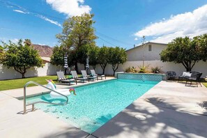 A swimming pool with lounge chairs and umbrellas, surrounded by trees and a building. - Adorable 4-bedroom house in La Quinta with private pool and mountain views! (La Quinta)