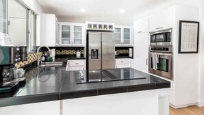 Una cucina moderna con mobili bianchi, un frigorifero in acciaio inossidabile, un forno a microonde e un forno.