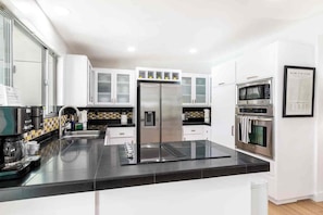 A modern kitchen with white cabinets, a stainless steel refrigerator, a microwave, and an oven. - Adorable 4-bedroom house in La Quinta with private pool and mountain views! (La Quinta)