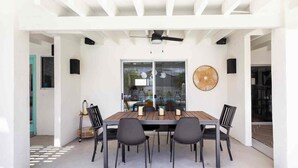 Un'area pranzo all'aperto con tavolo e sedie in legno, una ventola a soffitto e una grande finestra con vista.