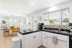 A modern kitchen with a black countertop, white cabinets, and a window with a view of a building. - Adorable 4-bedroom house in La Quinta with private pool and mountain views! (La Quinta)
