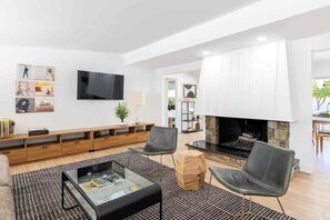 A modern living room with a fireplace, a flat-screen TV, and a seating area with chairs and a coffee table. - Adorable 4-bedroom house in La Quinta with private pool and mountain views! (La Quinta)