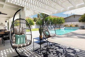 A poolside area with two hanging chairs, a small table, and a patterned rug. - Adorable 4-bedroom house in La Quinta with private pool and mountain views! (La Quinta)