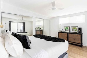 Een moderne slaapkamer met een groot bed, een kast, een spiegel en een plafondventilator.