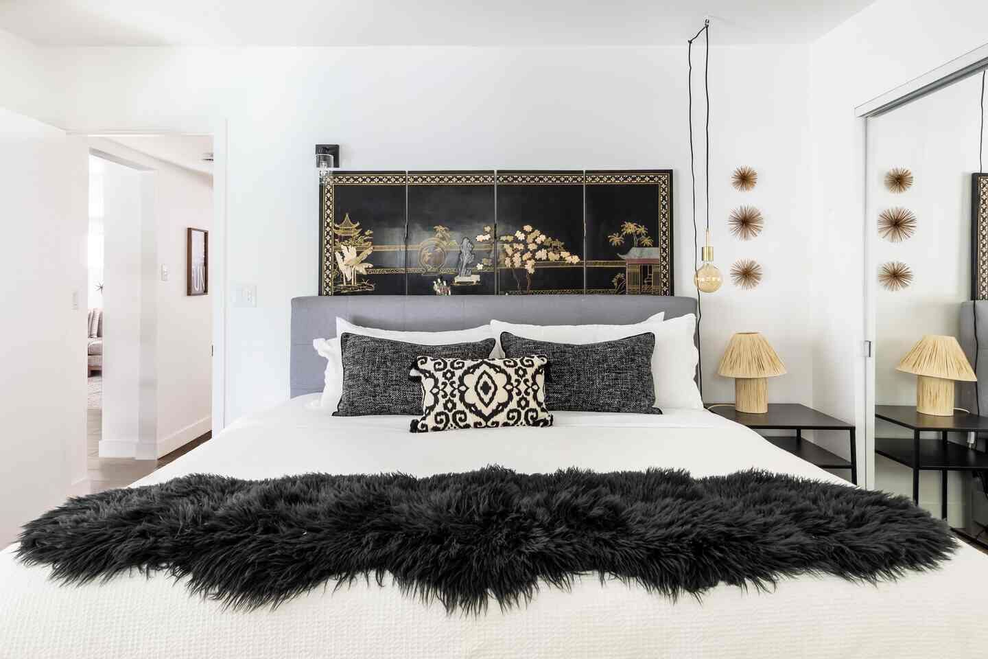 A modern bedroom with a large bed, decorative wall mirrors, and a black furry throw.