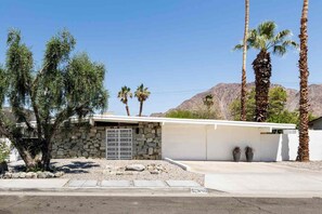 A modern house with a stone facade, a metal gate, and palm trees in the background. - Adorable 4-bedroom house in La Quinta with private pool and mountain views! (La Quinta)