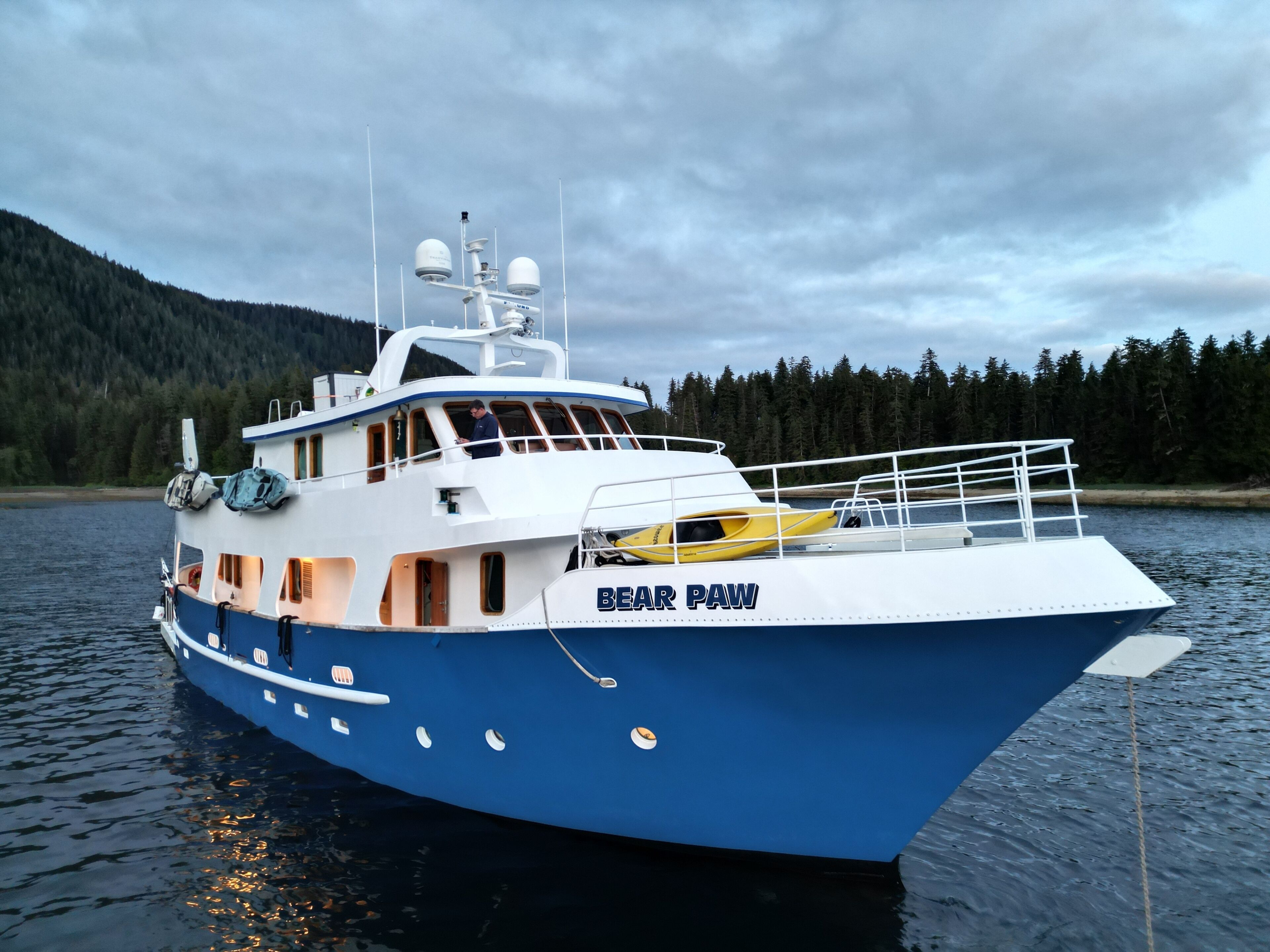 Un grand bateau appelé « BEAR PAW », doté d’une cabine, d’un pont et d’une petite cabine contenant un petit bateau jaune.
