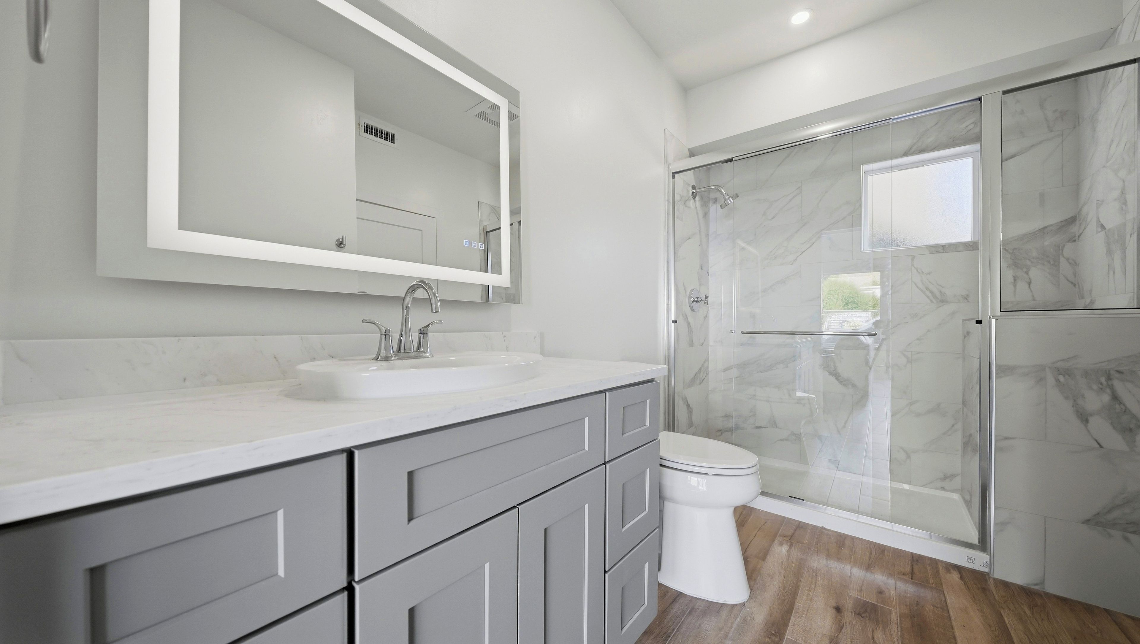 Une salle de bain moderne avec un lavabo en marbre, un grand miroir, des toilettes et une douche à parois de verre.