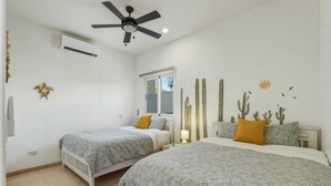 A bedroom with two beds, a ceiling fan, an air conditioner, and a window with a view. - Cerritos Beach Poolside Retreat / 2BR + BBQ (El Pescadero)