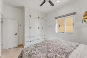 Un dormitorio con cama, armario, ventilador de techo, ventana y puerta.