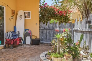 Eine Terrasse mit Surfbrettern, einem Wagen voller Taschen und verschiedenen Kübelpflanzen.