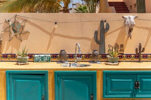 Una cocina con armarios turquesa, un lavamanos y decoración de cactus en la pared.
