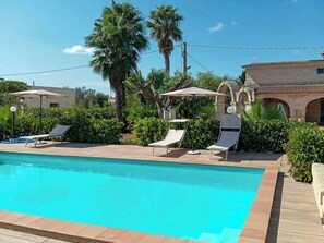 Ein Swimmingpool mit Liegestühlen und Sonnenschirmen, umgeben von Grünflächen und Steinarchitektur.