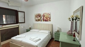 Un dormitorio con cama, escritorio, silla, ventilador de techo y obras de arte en la pared.