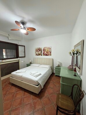 Ein Schlafzimmer mit einem Bett, einem Schreibtisch, einem Stuhl, einem Deckenventilator und Kunstwerken an der Wand.