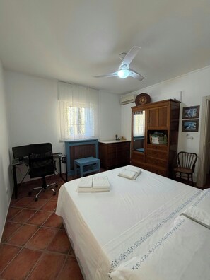 Ein Hotelzimmer mit Bett, Schreibtisch, Stuhl, Kleiderschrank und Deckenventilator.