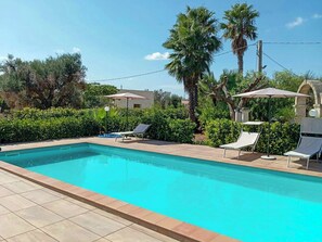 Ein rechteckiger Swimmingpool mit gefliesten Rändern, umgeben von einer Terrasse mit Liegestühlen und Sonnenschirmen.
