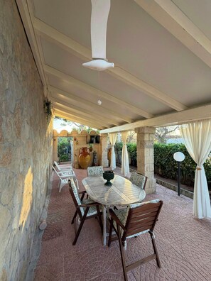 Eine Terrasse im Freien mit rundem Tisch und Stühlen, Steinmauern und einem Deckenventilator.