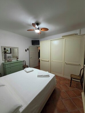 Ein Schlafzimmer mit Bett, Kommode, Stuhl, Kleiderschrank und Deckenventilator.