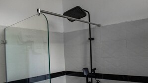 Dutxa amb envà d'estic, plat de dutxa manual i paraula per penjar tovalloles.