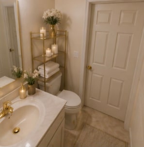 Ein Badezimmer mit goldfarbenem Waschtisch, weißem Waschbecken und Toilette. Ein Regal mit Kerzen und Handtüchern.