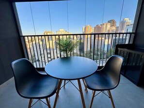 Ein Balkon mit rundem Tisch und zwei Stühlen, mit Blick auf eine Skyline aus hohen Gebäuden.