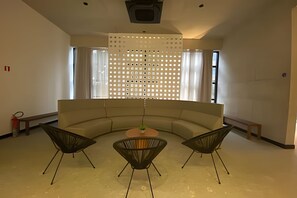 Ein modernes Interieur mit einer gebogenen Couch, drei schwarzen Stühlen, einem kleinen Tisch und einem dekorativen Raumteiler.