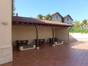 A covered patio area with tiled flooring, outdoor seating, and a building in the background. - Apartamento Anas - apartment in Nueva de Llanes, Northern Spain (Llanes)