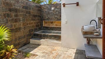 Un baño moderno con pared de piedra, un lavamanos y un escalón pequeño que conduce a la zona de ducha.