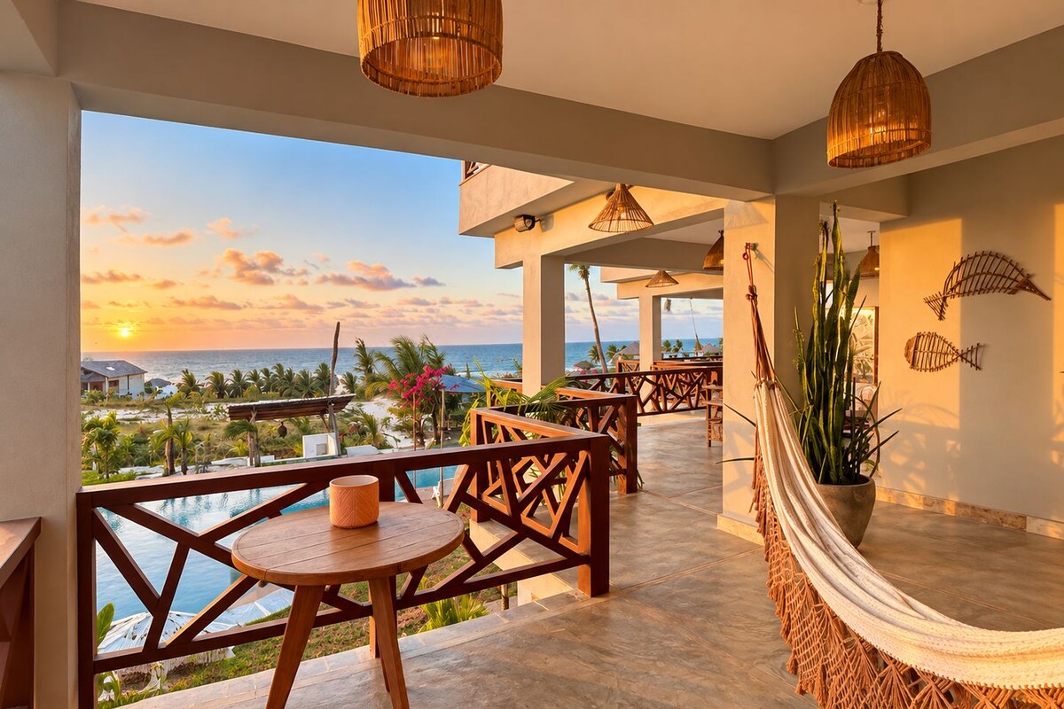 A balcony with a view of the ocean, wooden furniture, and a hammock.