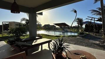 A sunlit outdoor seating area with a pool view, lounge chairs, and a wooden table.