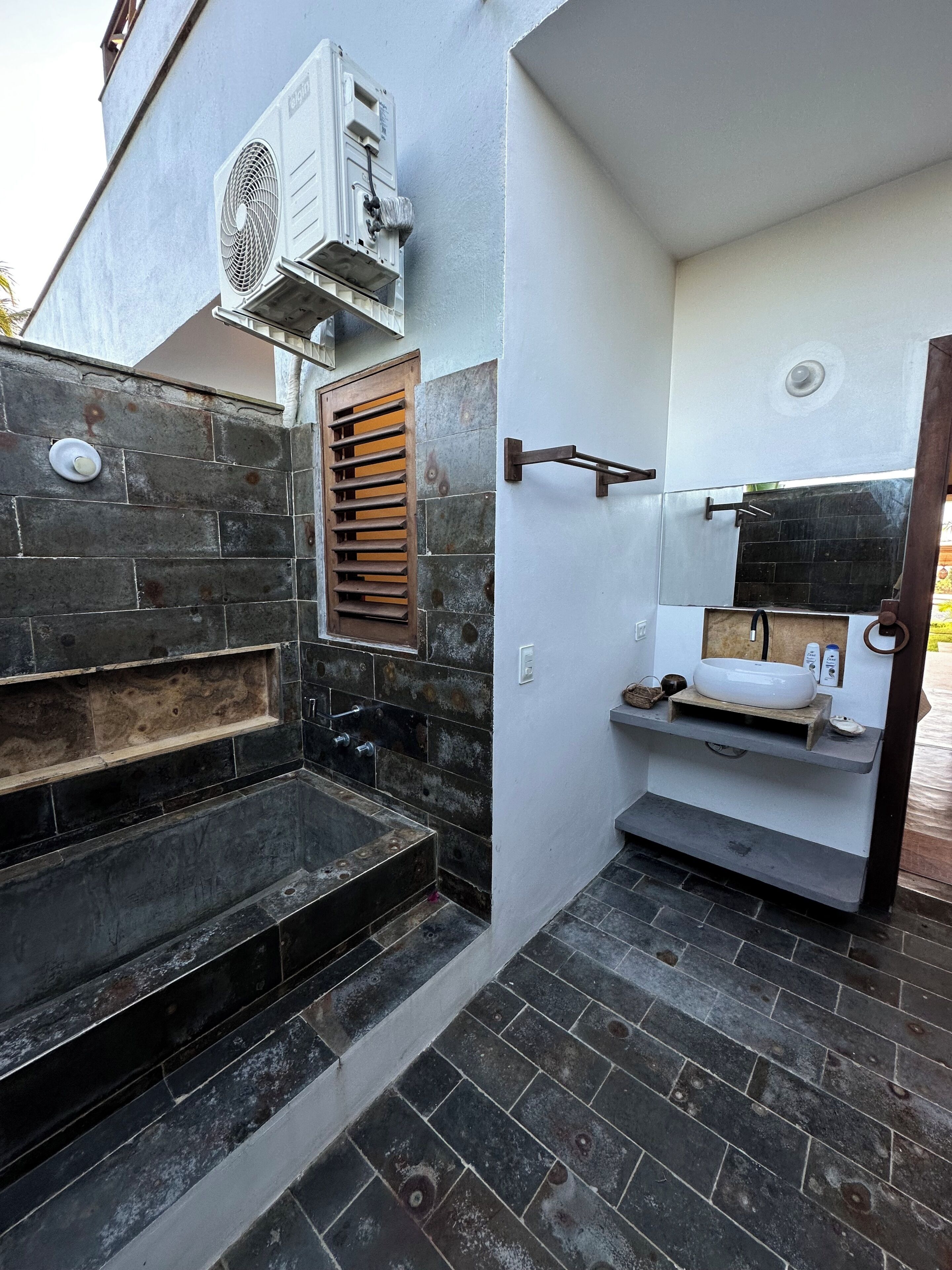 Un baño con pared de piedra, lavabo empotrado y ventana con persianas.