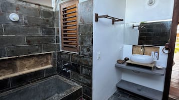 Un baño con pared de piedra, lavabo empotrado y ventana con persianas.