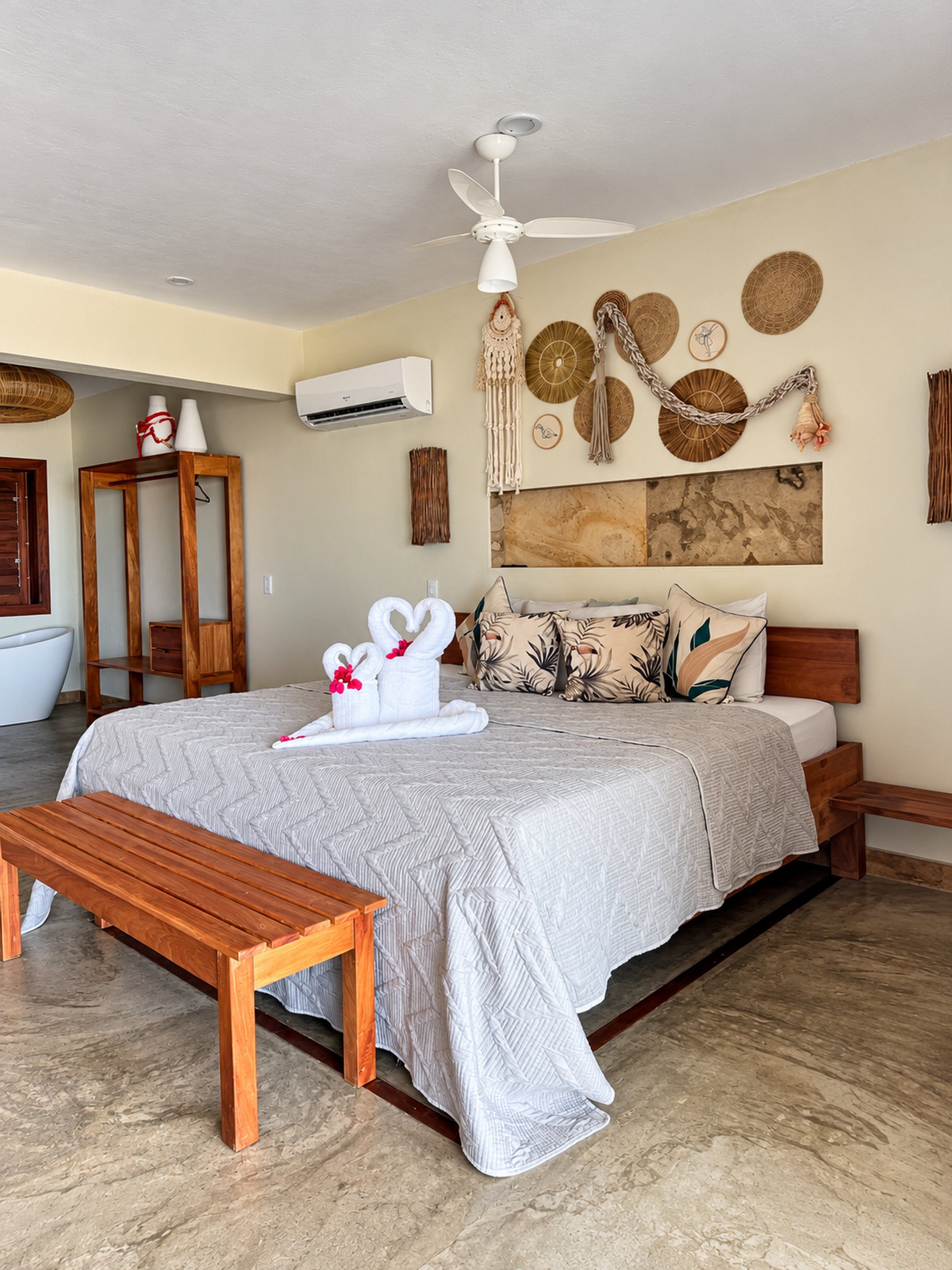 A hotel room with a bed, a wooden bench, a ceiling fan, and wall decor.