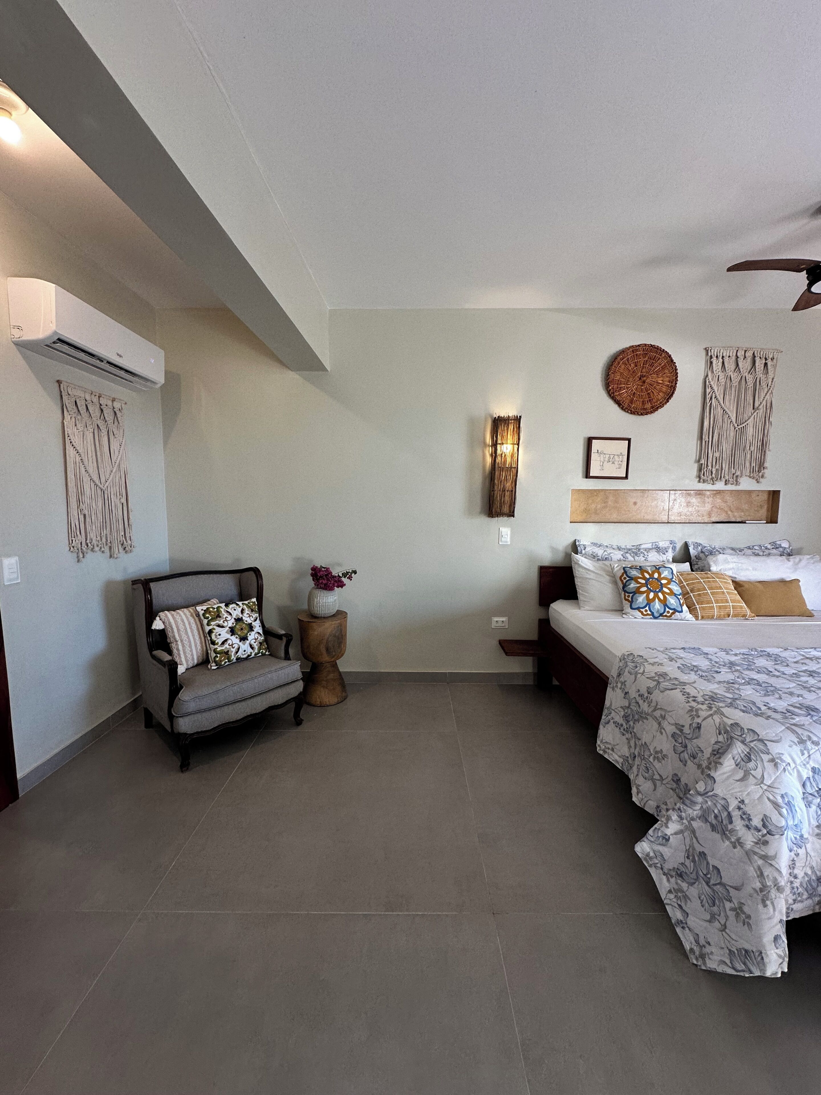 Un dormitorio con cama, sofá, aire acondicionado en la pared y un adorno mural.