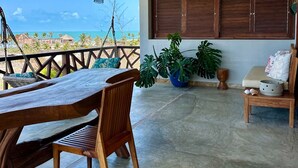 Un ampio balcone con tavolo e sedie in legno, una lampada a sospensione e vista sull'oceano.