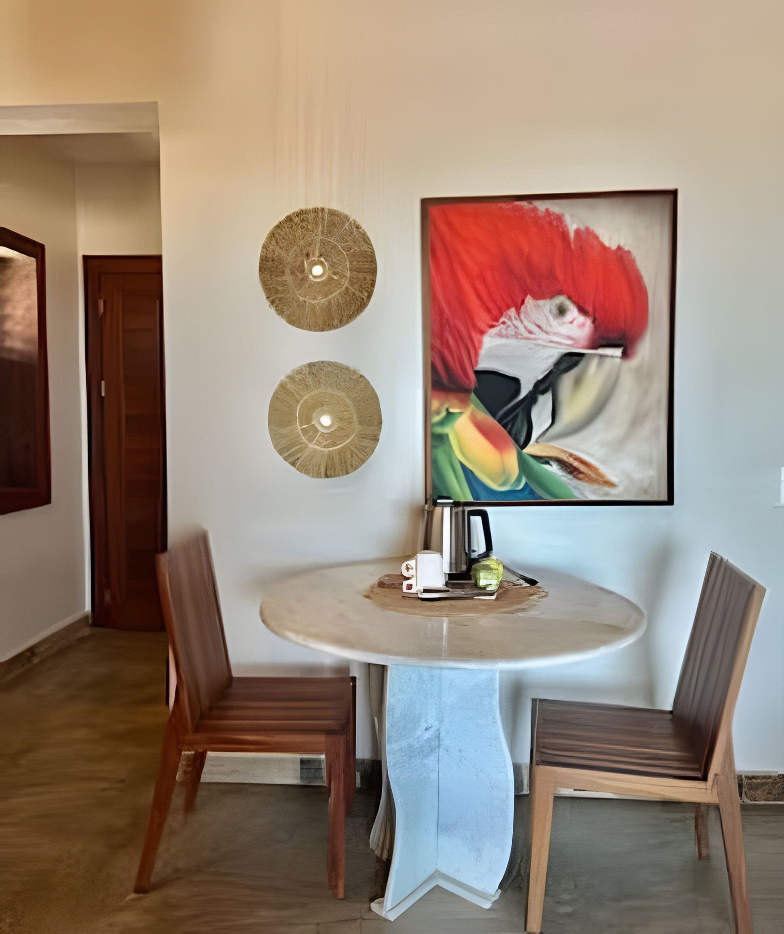A room with a round table, two chairs, a painting, and two wall-mounted light fixtures.