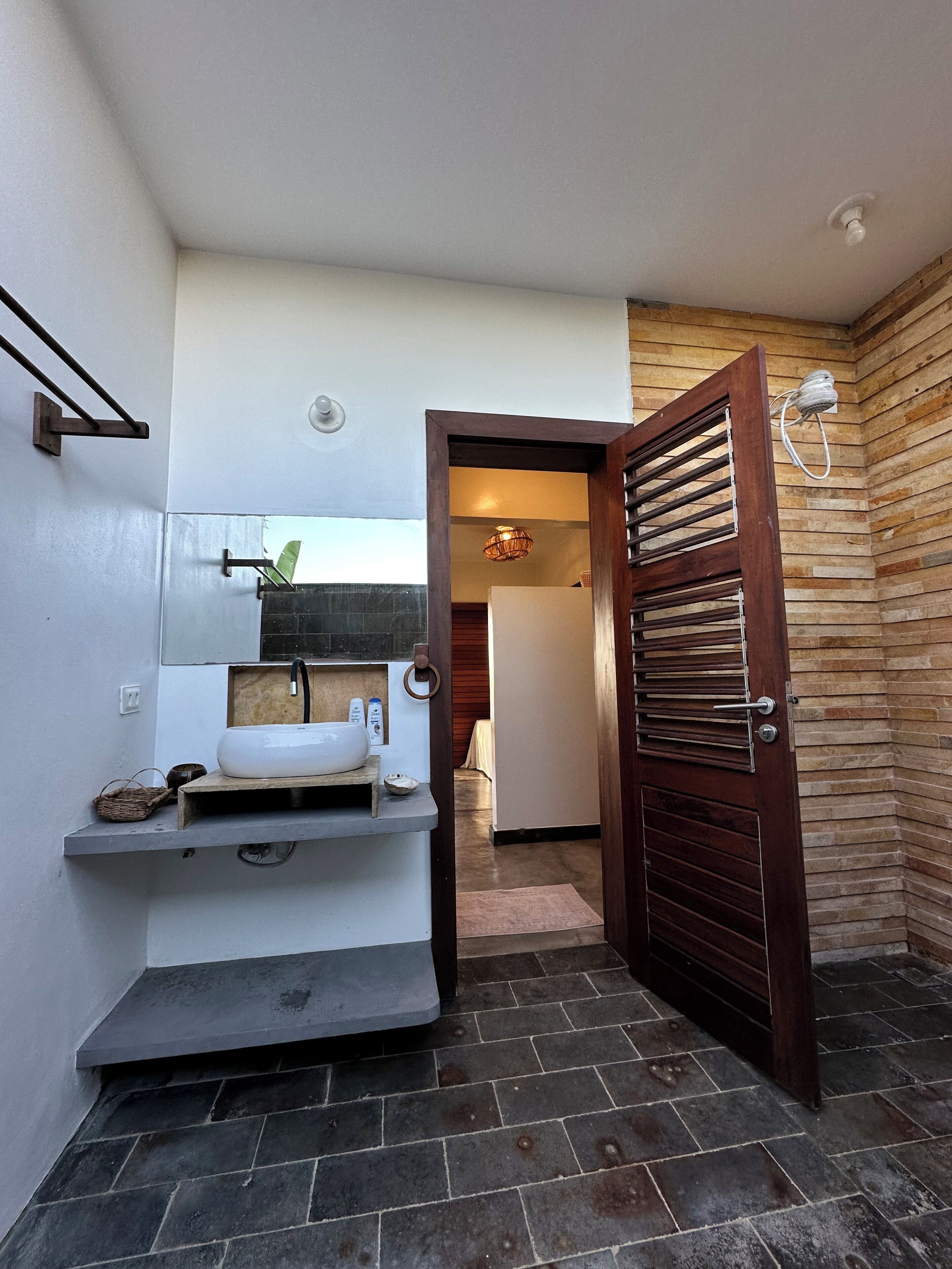 Une salle de bain avec un lavabo blanc, une étagère en bois et un porte-serviettes.