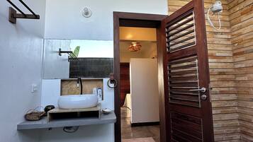 Une salle de bain avec un lavabo blanc, une étagère en bois et un porte-serviettes.