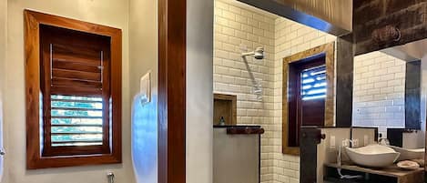 Un baño con inodoro, lavamanos, espejo y una planta en maceta.