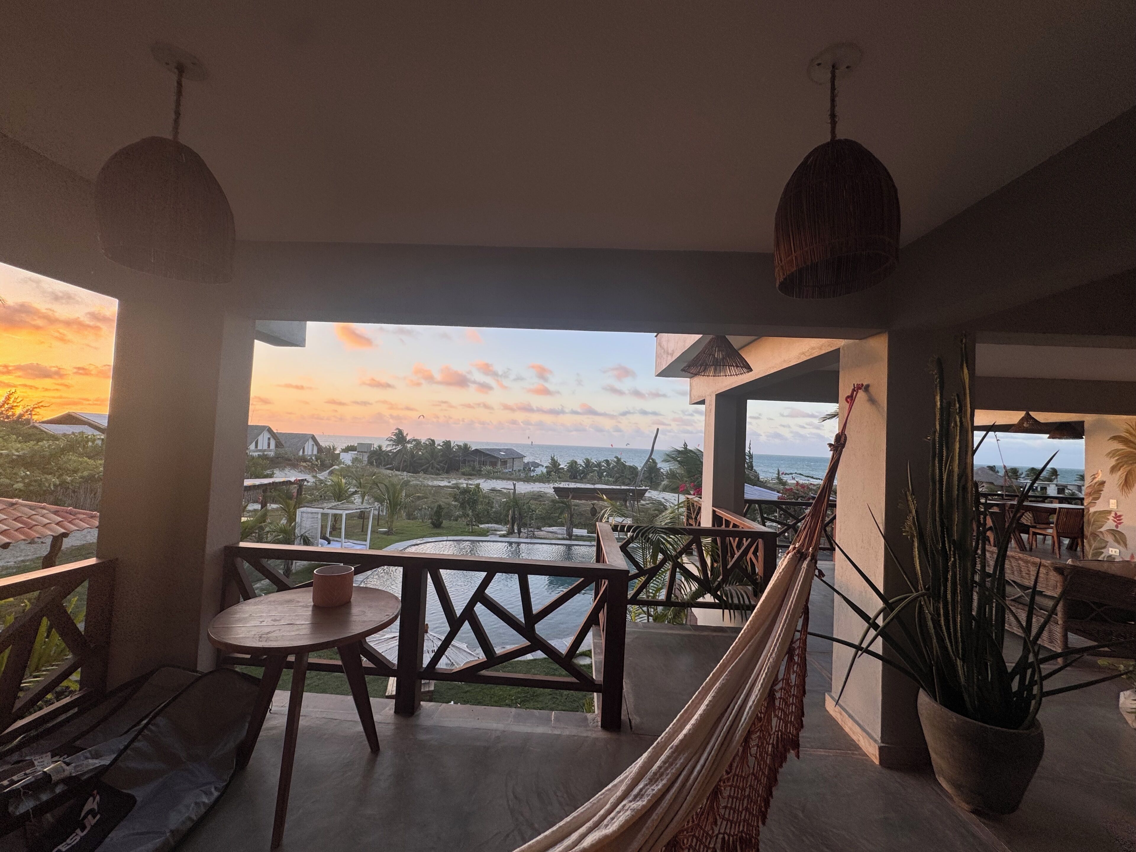 Una terraza con vista al océano, mesas, sillas y una hamaca.