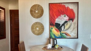 Zona pranzo con un tavolo rotondo, due sedie di legno, un quadro di un uccello e due elementi decorativi a parete.