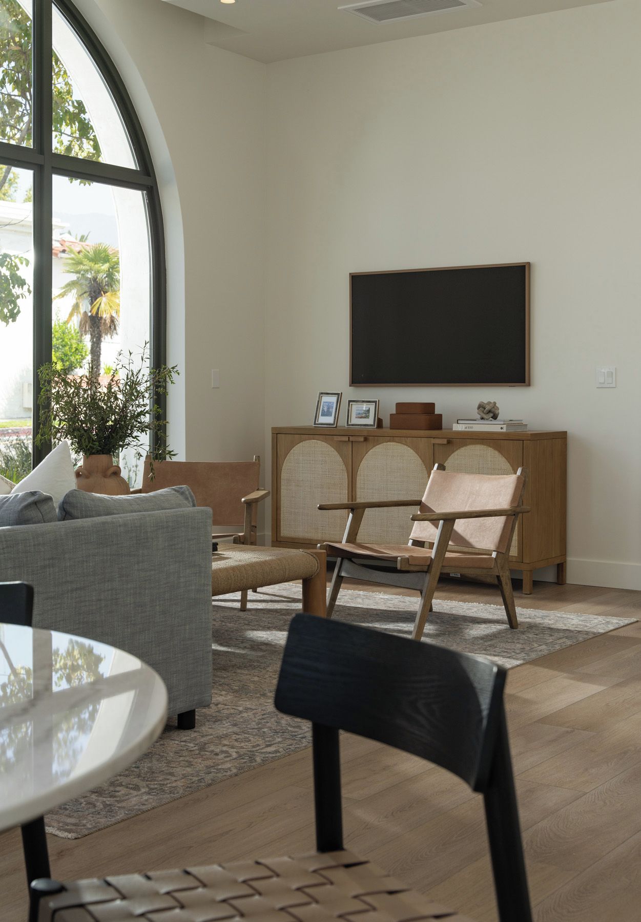 Una sala de estar moderna con un ventanal grande, un televisor de pantalla plana montado en la pared, un sofá, una mesa de centro y una silla.