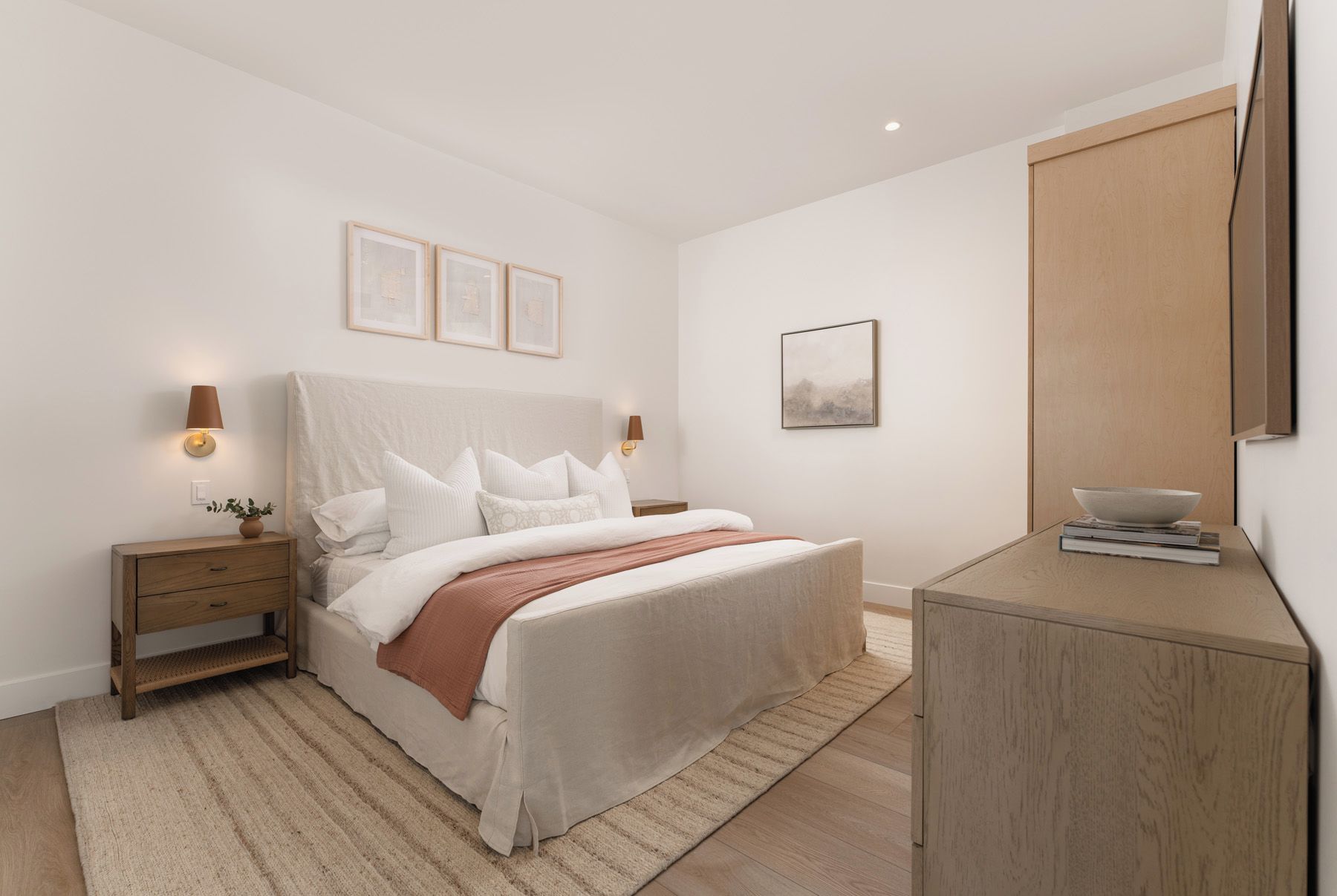 A minimalist bedroom with a bed, bedside tables, and a wooden cabinet.
