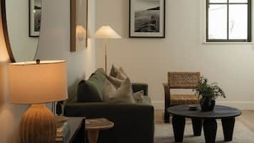 A modern living room with a sofa, a round coffee table, a side table with a lamp, and a chair. There is a large mirror on the wall and a framed picture above the sofa.