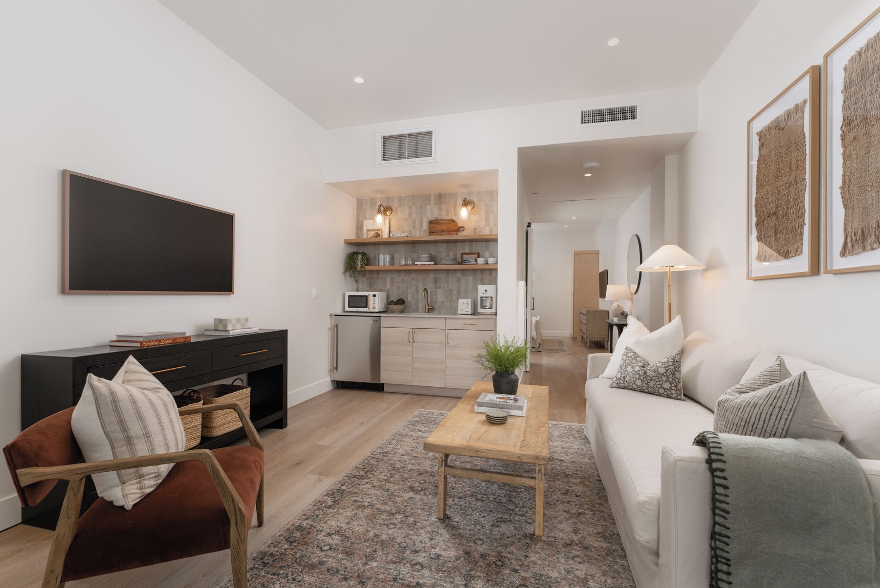 A modern living room with a sofa, a coffee table, a TV, and a dining area with a kitchen in the background.