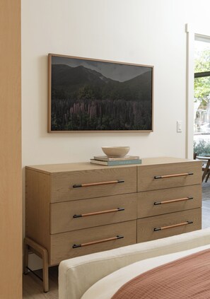 A bedroom with a wooden dresser, a bed, and a framed landscape painting on the wall.