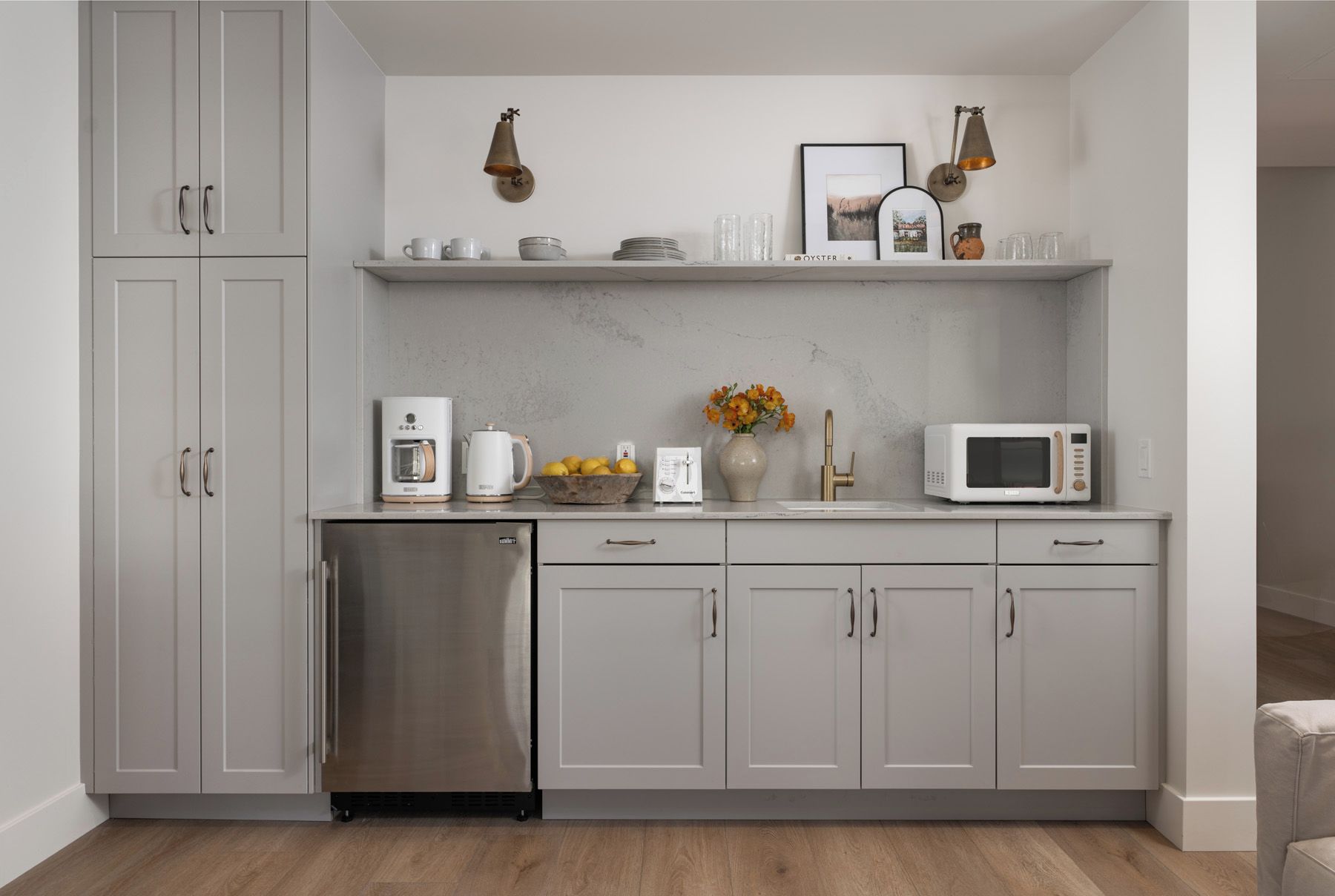 Una cocina moderna con gabinetes grises, lavavajillas de acero inoxidable, cafetera, hervidor, microondas y un florero con flores.