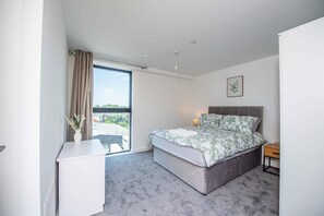 A bedroom with a bed, a desk, a nightstand, a window with a view, and a framed picture on the wall. - Sleek 2-Bed Salford Apartment near City Centre (Salford)