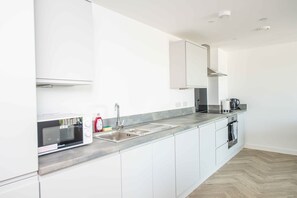A modern kitchen with white cabinets, a stainless steel sink, a microwave, and a coffee maker. - Sleek 2-Bed Salford Apartment near City Centre (Salford)